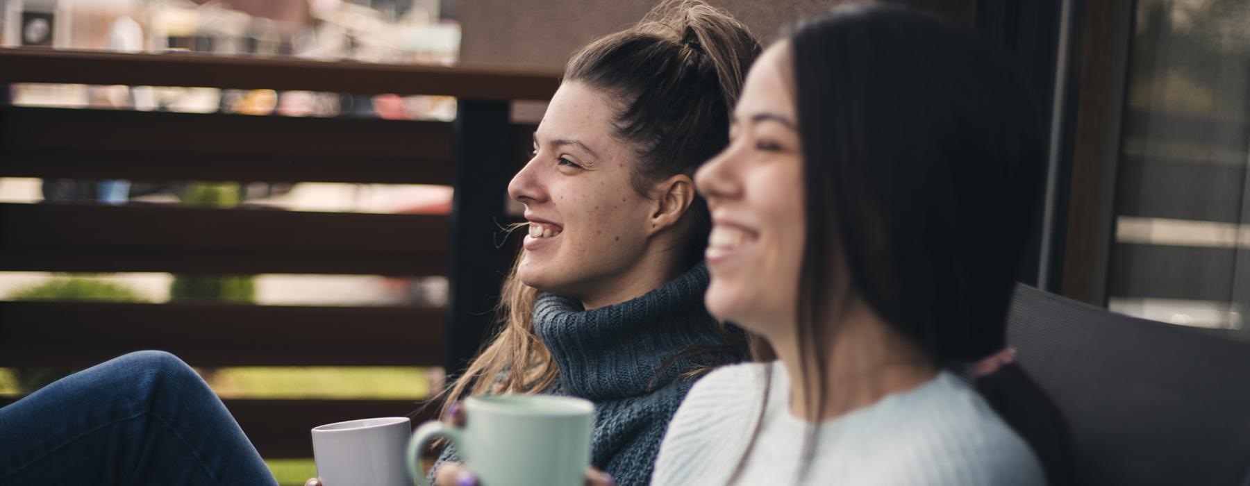 a couple of women sitting on a bench and drinking coffee